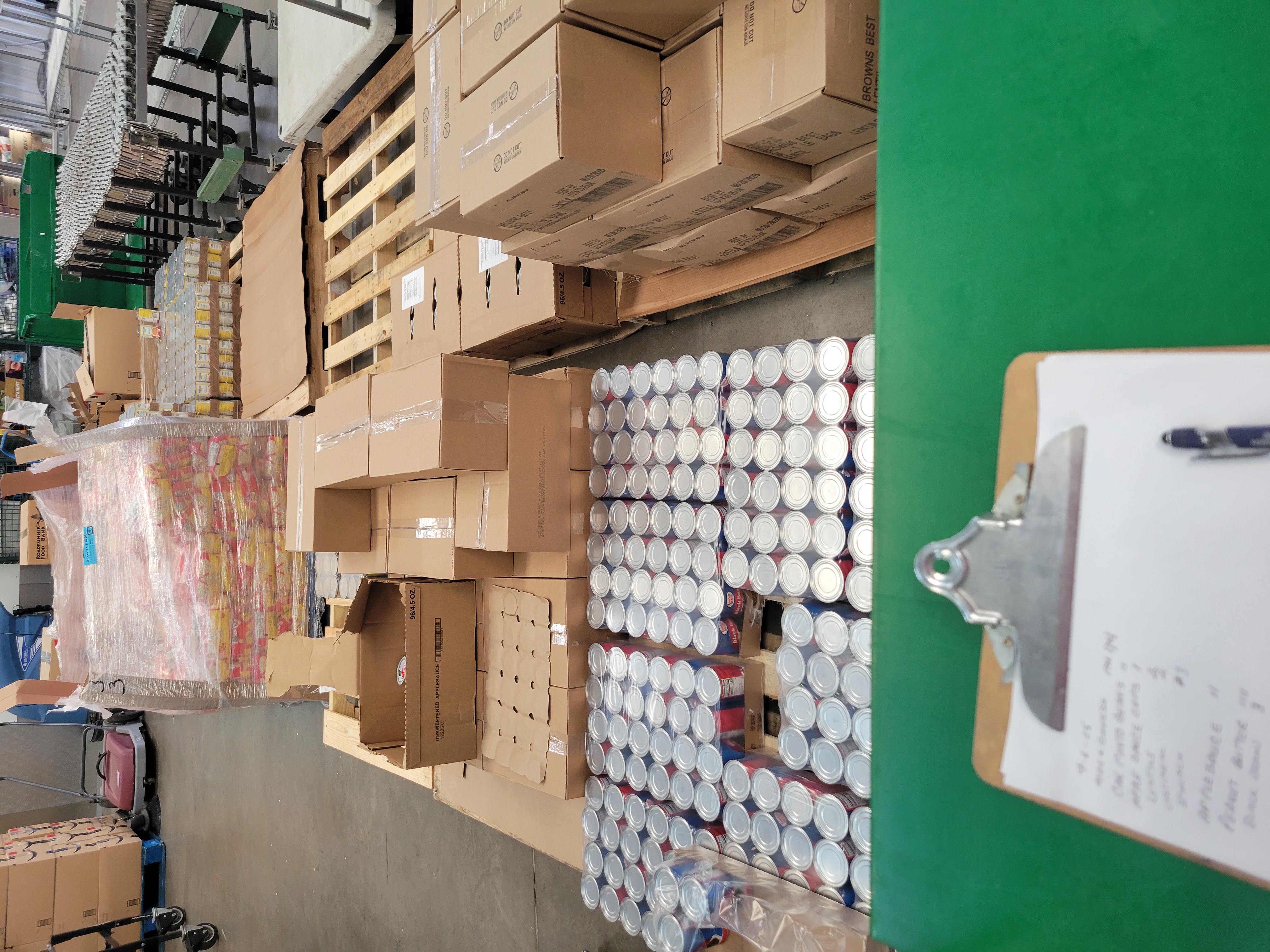 Clipboard with pen on a shelf cart with pallets of food behind it.